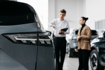 Car dealership scene featuring a male sales representative discussing vehicle features with a female customer, showcasing modern automotive sales environment with sleek vehicles