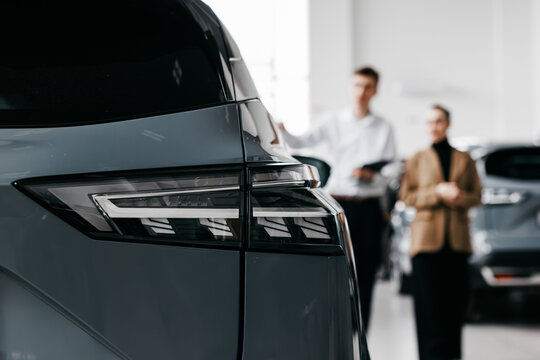 Modern car dealership interior showcasing sleek vehicle rear, with sales representatives engaging with customers, highlighting the car sales experience and customer service atmosphere