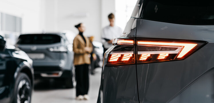 Modern car dealership interior showcasing sleek vehicles with a focus on a gray car's rear lights, highlighting the vibrant atmosphere of automotive sales and customer engagement