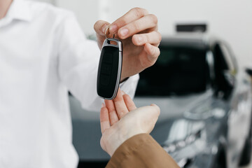 Man in white shirt handing over car keys to customer, showcasing successful car sale transaction in modern dealership environment with vehicles in background