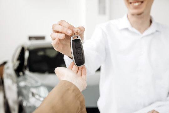 Smiling man in white shirt hands over car keys to customer in a modern car dealership, showcasing the excitement of purchasing a new vehicle with copy space