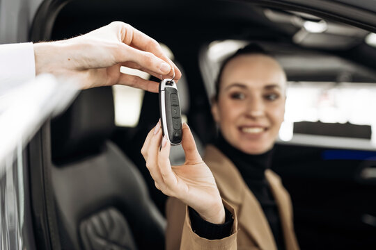 Smiling woman receiving car keys from salesperson inside dealership, showcasing excitement and satisfaction in a modern automotive sales environment with copy space - Powered by Adobe