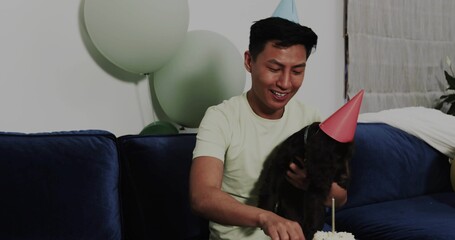 Man wearing blue party hat holding dog in party hat, celebrating cake at home, copy space