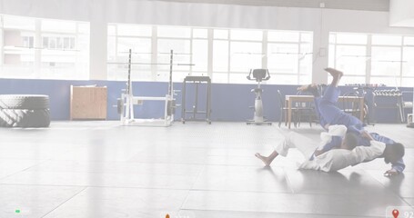 Grappling partners wearing gis on padded mats in martial arts gym, with large tire, copy space