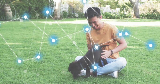 Asian man in mustard shirt sitting in park, petting puppy, with data overlay and fitness tracker