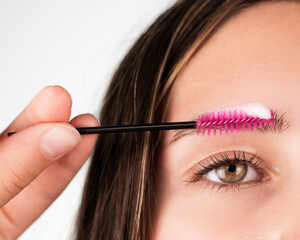A person uses a pink spoolie brush with foam to clean their eyebrow, shown in closeup detail. Suitable for beauty, skincare, makeup tutorials, and personal grooming content.