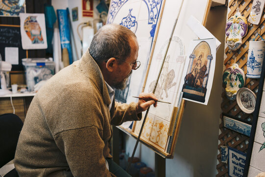 Andalusian ceramic craftsman painting traditional tiles in workshop