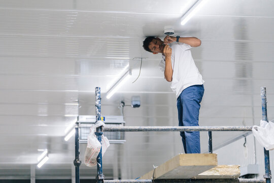Man installing security camera on warehouse ceiling