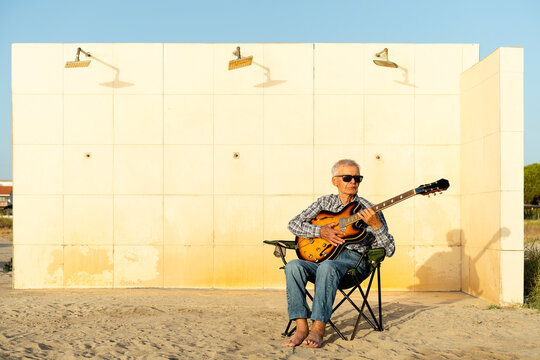 Senior man playing guitar at the beach in front of public showers