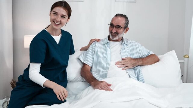 young nurse in uniform takes care of an elderly man, holding his hand and asking him about his condition and giving him encouragement. A nurse uses a stethoscope to check his pulse in a nursing home.
