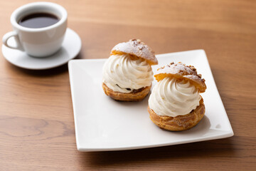 Cream puffs with whipped cream and a cup of coffee on a wooden table