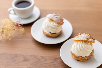 Cream puffs with whipped cream and a cup of coffee on a wooden table