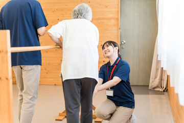 Senior woman using handrails for walking training and male and female occupational therapists and physical therapists assisting her
