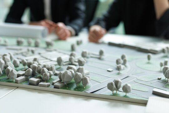 Close up of area model on foreground of partial architects at meeting