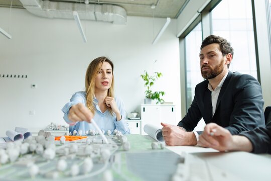 Focused architect pointing on residential area model to colleagues