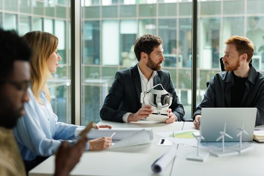 Team of architects discussing with company leader holding VR headset