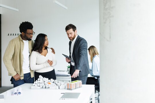Male realtor with tablet showing model of residential area to couple