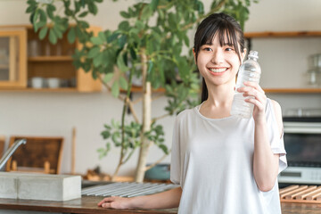 Young Asian woman drinking mineral water, water, sports drink in front of her kitchen
