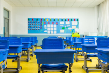 Empty classroom with blue desks and colorful bulletin board in modern school