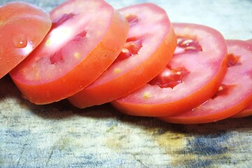 Fresh red tomato slices, solanum lycopersicum or lycopersicum esculentum on an old wooden cutting board photographed on the isolated white background