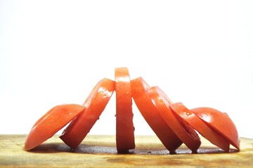 Fresh red tomato slices, solanum lycopersicum or lycopersicum esculentum on an old wooden cutting board photographed on the isolated white background