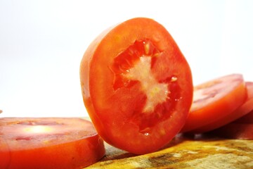 Fresh red tomato slices, solanum lycopersicum or lycopersicum esculentum on an old wooden cutting board photographed on the isolated white background