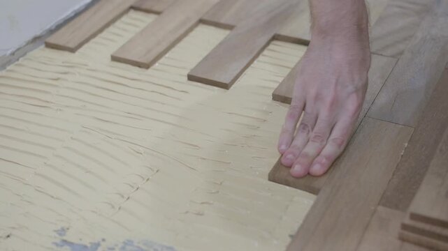 Close-up 4K horizontal video of hands installing iroko wood parquet with adhesive glue during DIY home floor renovation project