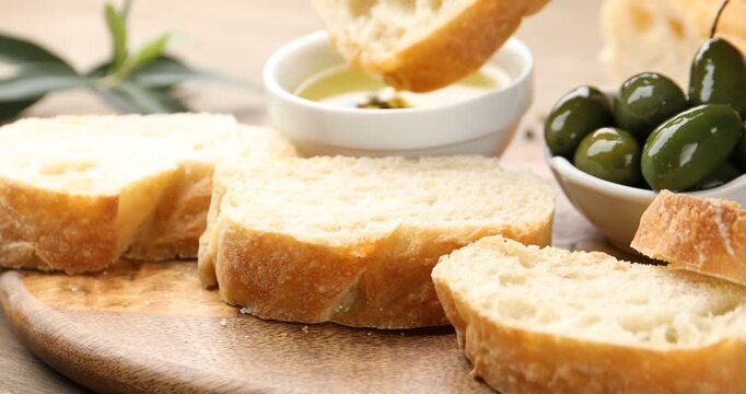 Woman dipping ciabatta slice into oil at wooden table, closeup