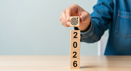Person holding wooden block with target symbol over stacked blocks reading 2026 leadership business goals finance inspiring future planning