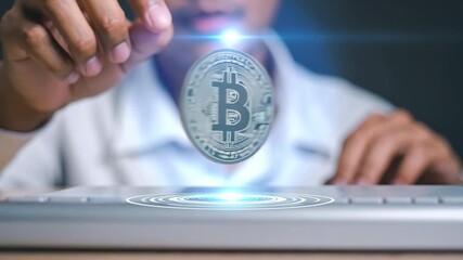 A person's hand interacts with a glowing holographic Bitcoin coin rising from a digital interface. - Powered by Adobe