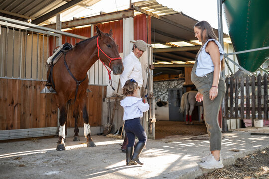 Three generations with horse in stable, grandfather, pregnant mother - Powered by Adobe