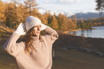 In a serene forest setting, a woman relaxes and embraces the beauty of autumn. Vibrant trees frame the calm lake as she enjoys her weekend of solo travel, taking in the fresh air.