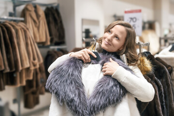 A white young beautiful woman of 30-35 dreamily clutches a winter coat with a fur collar. She dreams about this purchase. Winter fashion Christmas shopping and women's Christmas holiday shopping