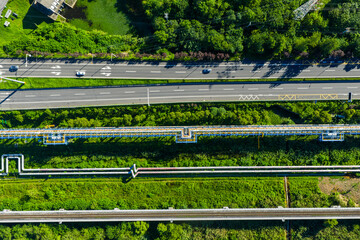 road with vehicles parallel to industrial pipelines and railway