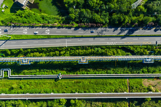road with vehicles parallel to industrial pipelines and railway