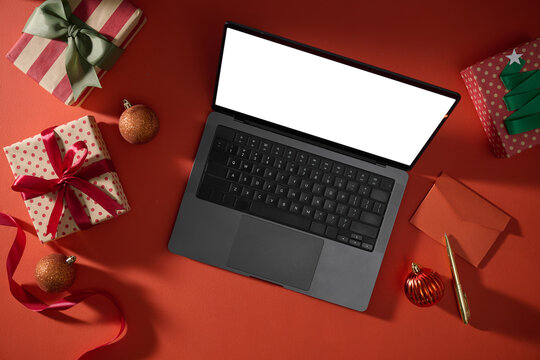 Christmas gifts and decorations surround a laptop computer on red