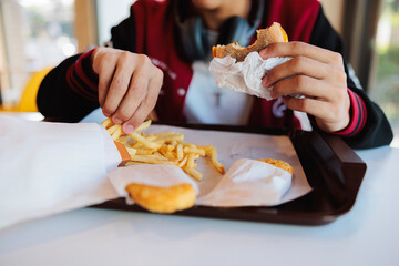 Person eating burger, fries, and hash browns on tray.