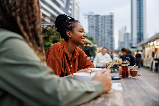 Friends enjoy noodles at an outdoor urban food market.