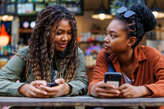 Two young women with phones at an outdoor cafe.