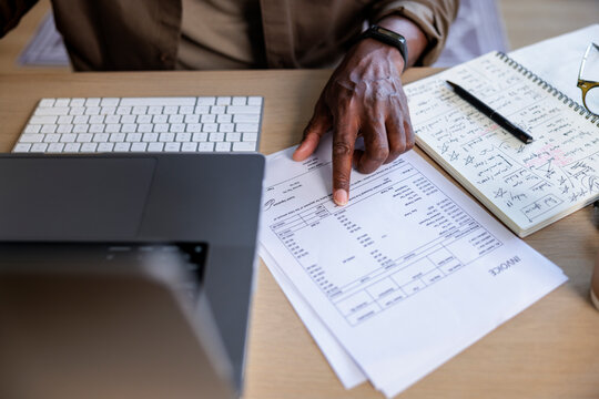 Man reviews invoice with laptop, keyboard, and notebook.