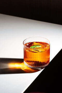 Amber cocktail with mint and ice casting golden shadow on table