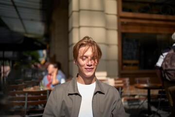 Smiling Young Man Enjoying a Sunny Day at a Bustling Cafe