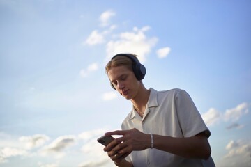 Enjoying Music Outdoors With Headphones Under a Blue Sky