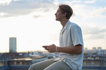 Young Man Enjoying Sunset While Using Smartphone on Rooftop