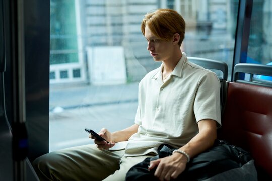 Young Man Absorbed in Mobile Phone While Riding City Bus