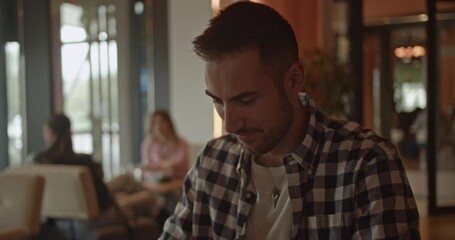 Focused businessman engages in an important phone call while seated in a contemporary cafe lounge. Other professionals are subtly visible in the background, highlighting a dynamic business setting. - Powered by Adobe