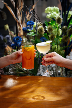 Two hands holding cocktails with floral background
