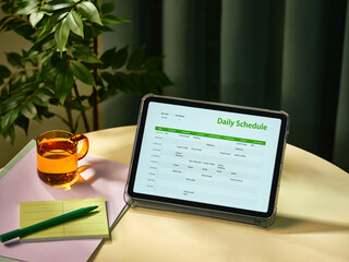 A digital tablet displays a daily schedule with a cup of tea on desk