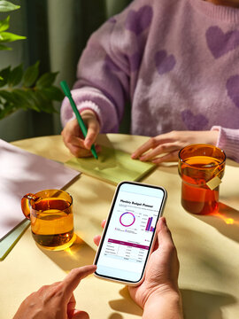 Someone checks the monthly budget app on a phone, with another person