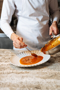 Chef plating red soup with ladle onto white dish